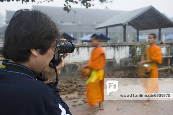 Photographer Taking Pictures Of Novice Monks Out Collecting Alms At Dawn.