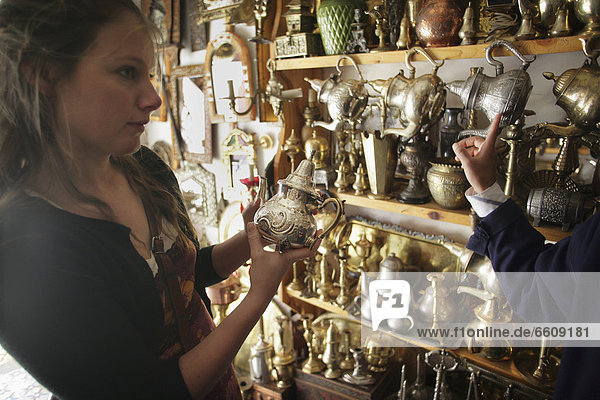 Young Woman Bargaining For A Silver Teapot In A Market Stall In The Souk.