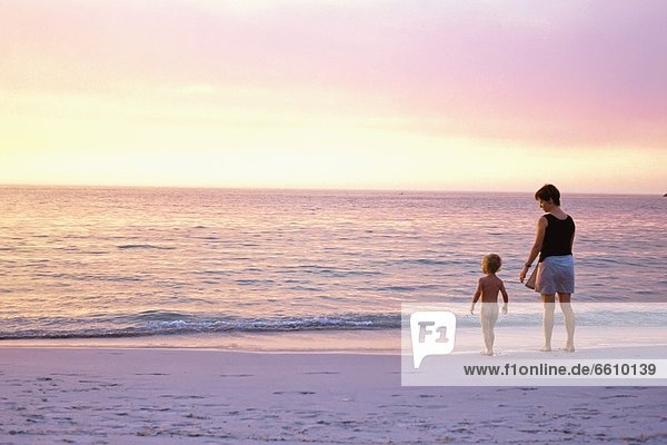 Mother And Son (2-3 Years) Standing On Beach At Sunset  Rear View
