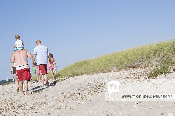 Family Walking By Grassy Sand Dunes On Beach