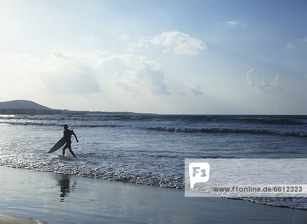 Man with surfboard running on beach
