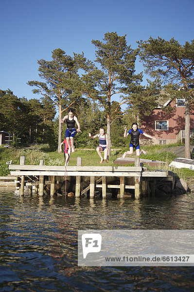 Children (8-15) jumping off pier into sea Foglo Aland Islands Finland