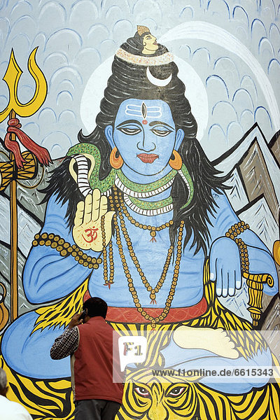 Guy Using Mobile Phone Passing Mural Of Shiva  One Of The Most Famous Hindu Gods/Deities Painted On A Tower At Dashashwamedh Ghat The Most Famous And Central Bathing Ghat. The Culture Of Varanasi Is Closely Associated With The River Ganges And The River S Religious Importance.It Is The Religious Capital Of India And An Important Pilgrimage Destination.Varanasi  Also Known As Benares  An Ancient City  One Of The World S Oldest Continually Inhabited Cities  Situated On The Left/West Bank Of The Sacred Ganges River. Regarded As Holy By Hindus  Buddhists  And Jains.  Uttar Pradesh State  India  Asia. © Paul Quayle / Axiom