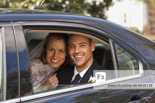 Caucasian bride and groom in back seat of car