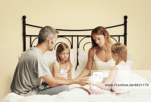 Family Holding Hands And Praying Together In Bed
