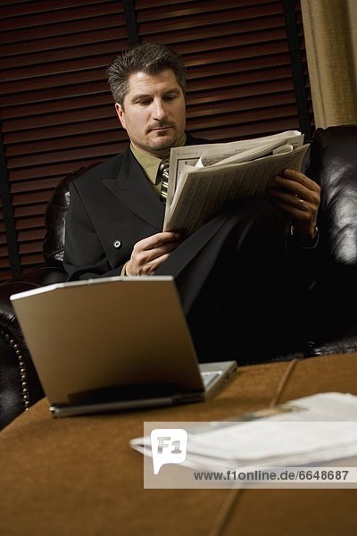 Businessman Reading The Newspaper With His Laptop