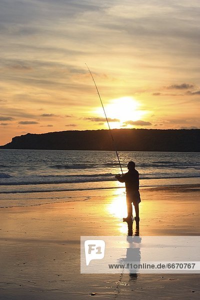 Silhouette Of Person Fishing On A Beach
