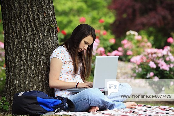 A Teenage Girl Working On Her Laptop Computer Under A Tree