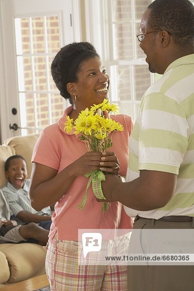A Husband Giving Flowers To His Wife With The Son Watching