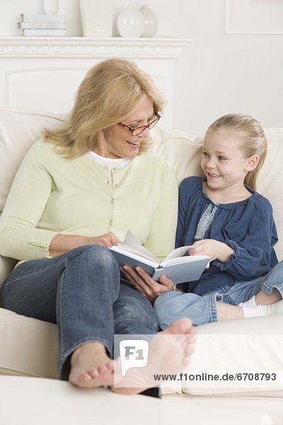 Grandmother reading to young granddaughter on sofa