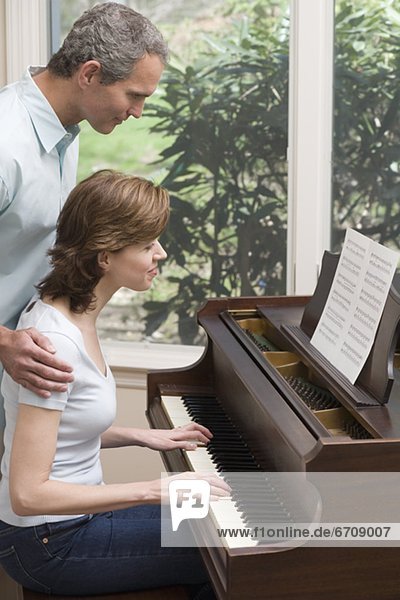 Woman playing piano with man watching