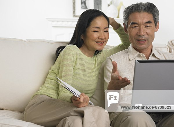 Middle-aged Asian couple sitting on sofa with laptop