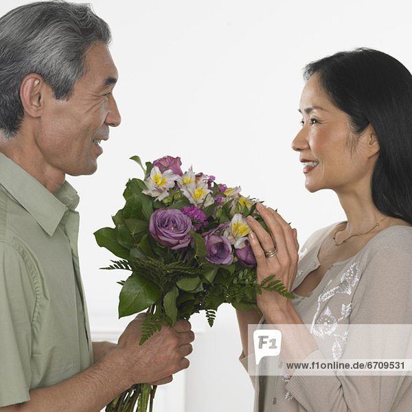 Asian man giving Asian woman bouquet of flowers