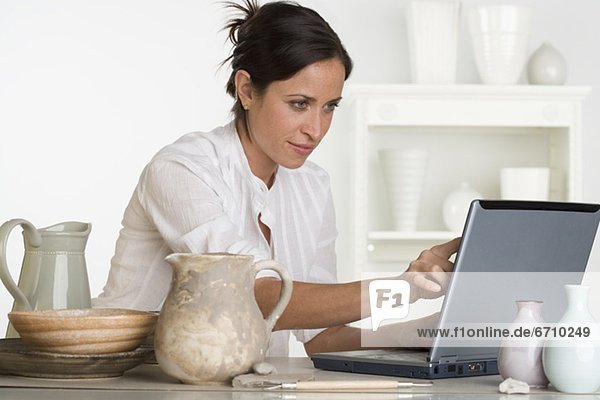 Woman using laptop next to pottery