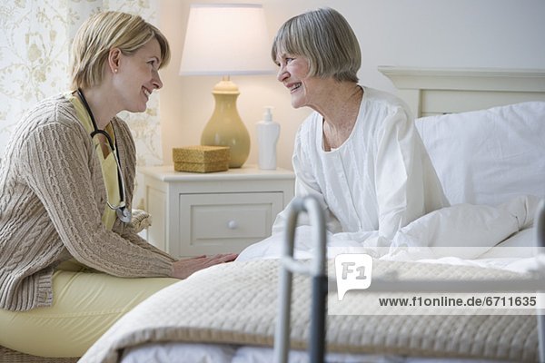 Nurse talking to senior woman in bed