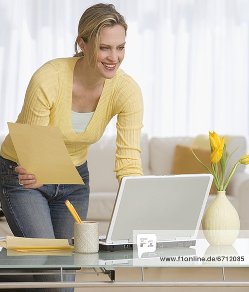 Woman holding paper and looking at laptop