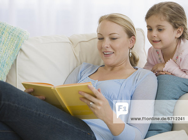 Mother reading to daughter on sofa