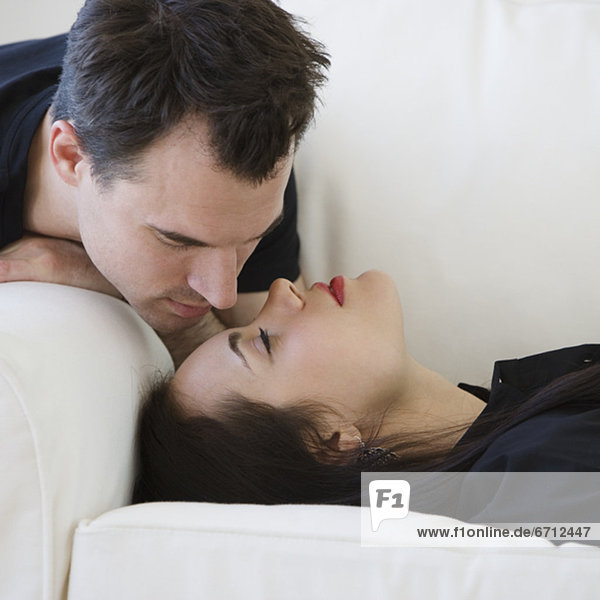 Man leaning over girlfriend on sofa