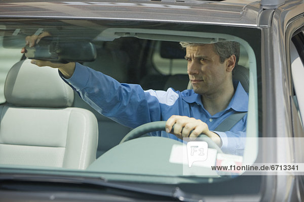 Man adjusting rear view mirror in car