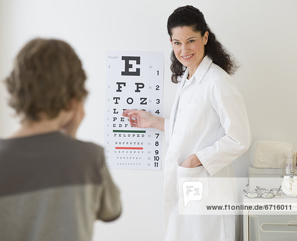 Hispanic female doctor pointing at eye chart for child
