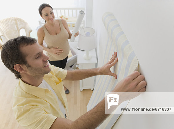 Pregnant Hispanic couple hanging wall paper in nursery