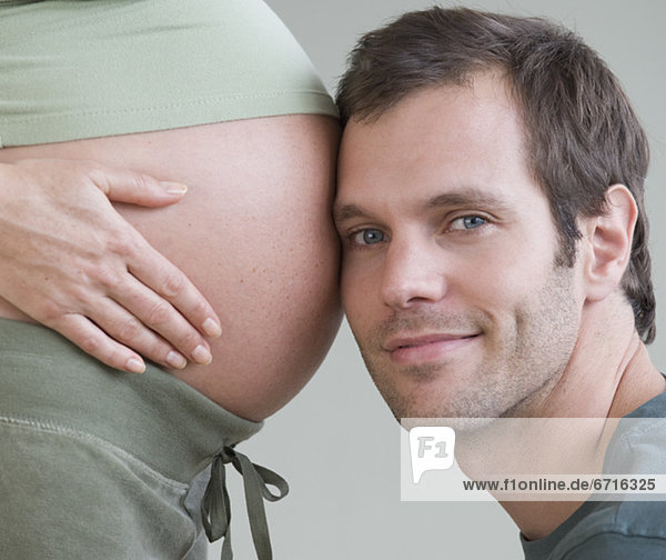 Hispanic man resting head on pregnant wifeÕs belly