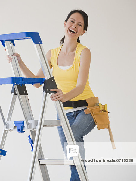 Woman wearing tool belt climbing ladder