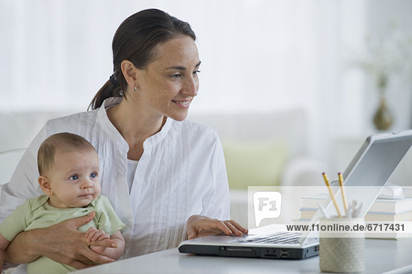 Mother working on laptop and holding baby son
