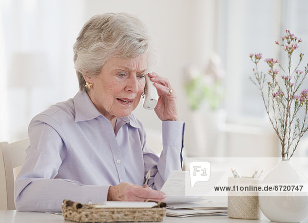 Senior woman paying bills and talking on phone