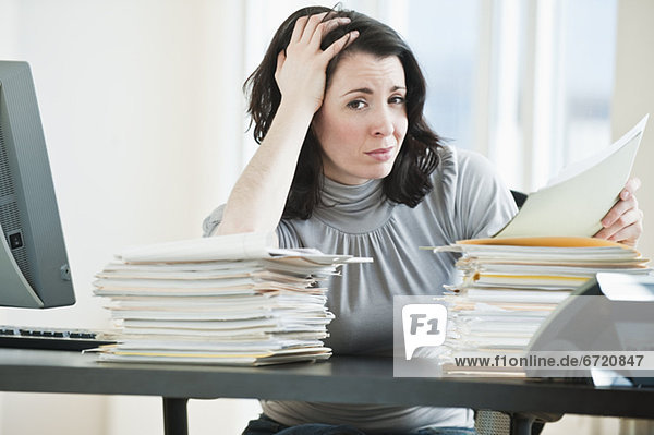 Stressed business woman holding paperwork in office