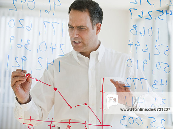 Mature businessman drawing line graph on transparent glass wall