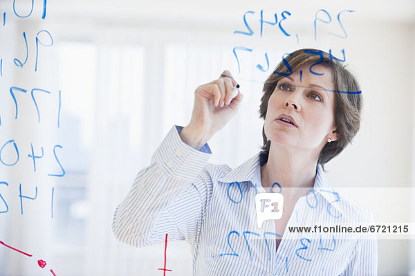 Mature businesswoman writing numbers on transparent glass wall
