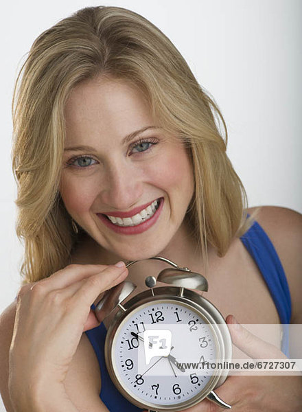 Happy blond woman holding an alarm clock