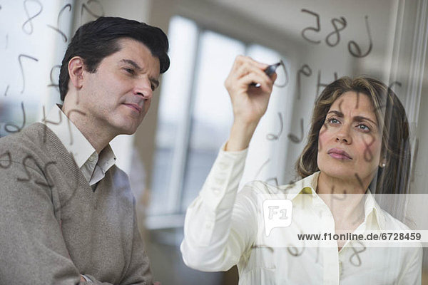 USA  New Jersey  Jersey City  Businessman and woman writing calculations on glass