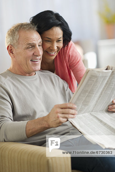 Mature couple sitting in armchair  reading newspaper