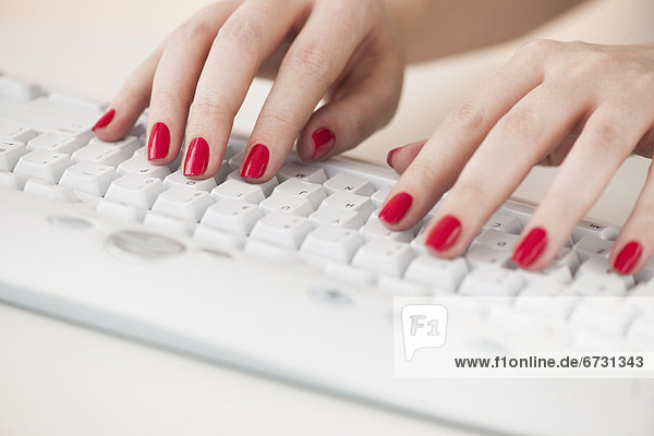 Close up of woman's fingers with red nail polish typing on computer keyboard