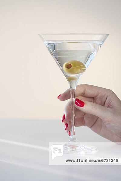 Close up of woman's hand with nail polish holding martini glass with olive