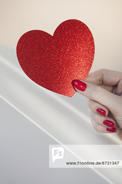 Close up of woman's fingers with red nail polish holding red heart