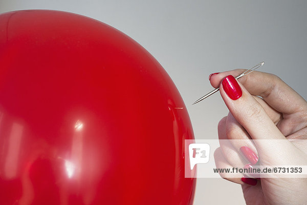 Close up of red balloon and woman's hand holding needle