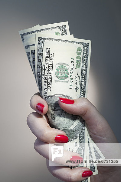 Close up of woman's hand with red nail polish holding bunch of dollar banknotes