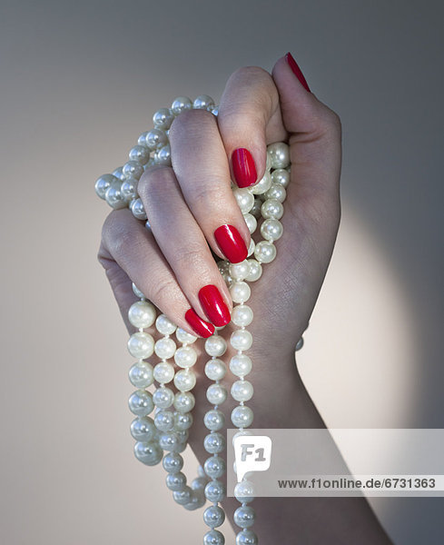 Close up of woman's hands with red nail polish holding pearls