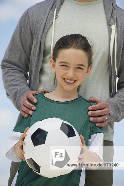 Girl (8-9) holding soccer ball  with father behind