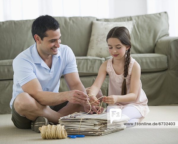 Father and daughter (8-9) wrapping up wastepaper bundle