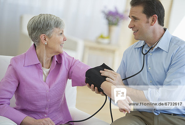 Smiling man taking senior woman's blood pressure