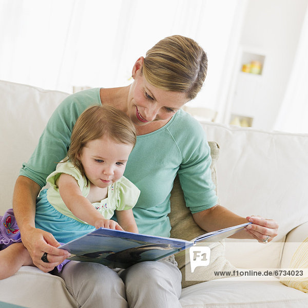 Mother with daughter (2-3) reading book on sofa