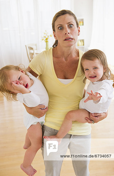Mother holding crying daughters (2-3) and making facial expression
