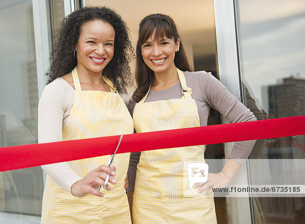 Two female business owners cutting red ribbon