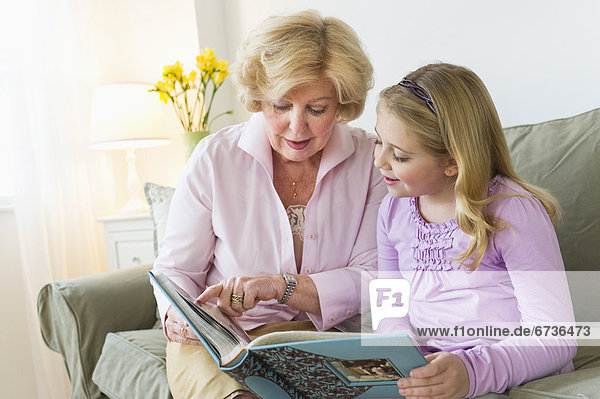 Grandmother with granddaughter (8-9) reading on sofa