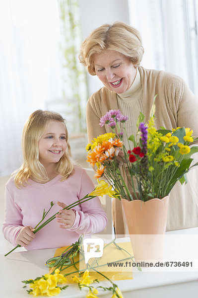 Smiling senior woman arranging flowers with granddaughter (8-9)