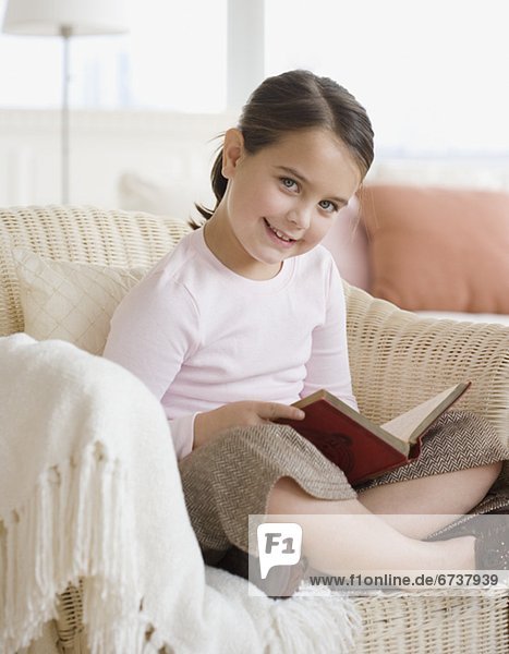 Portrait of girl holding book in chair